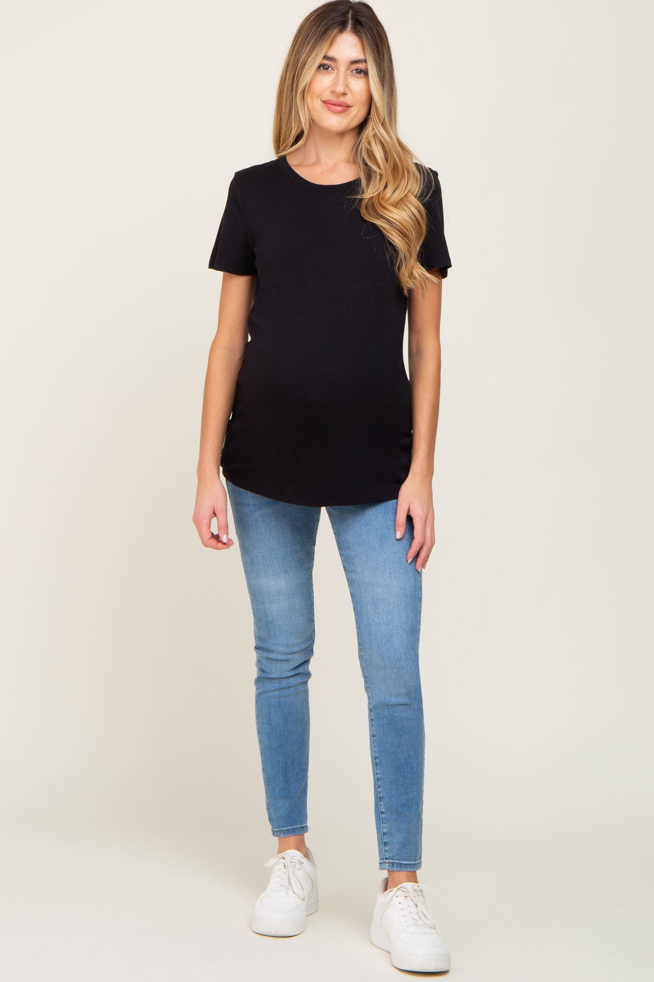 woman wearing a black short sleeve maternity top and blue skinny jeans, showcasing her baby bump