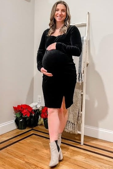 woman wearing a black velvet maternity dress with a thigh-high slit, holding her baby bump