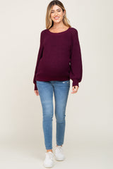 woman wearing a burgundy oversized maternity sweater and blue skinny jeans, showing her baby bump