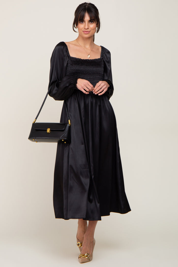 woman wearing a black satin long sleeve dress with a smocked bodice and carrying a black handbag