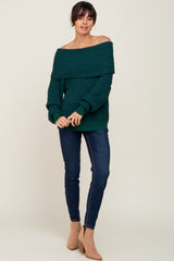 woman wearing a dark green off-the-shoulder knit sweater with dark blue skinny jeans and tan ankle boots