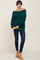 woman wearing a dark green off-the-shoulder knit sweater with dark blue skinny jeans and tan ankle boots