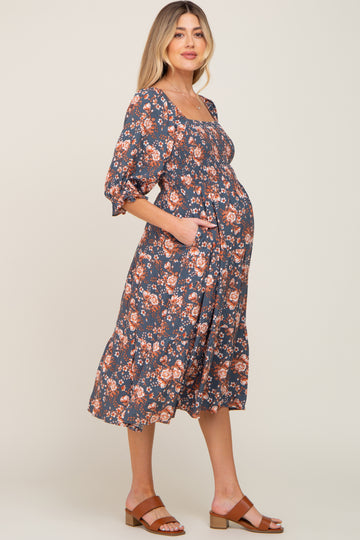 Pregnant woman wearing a navy blue floral smocked maternity midi dress with puff sleeves and brown sandals