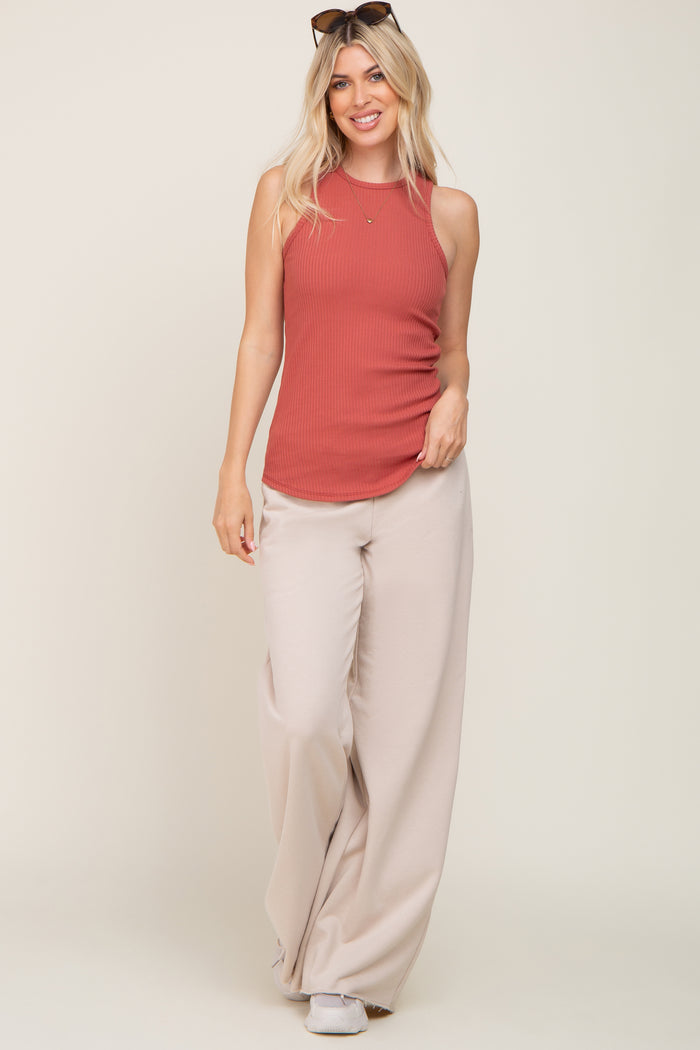 woman wearing a rust-colored ribbed tank top and beige wide-leg pants, posing with sunglasses on her head