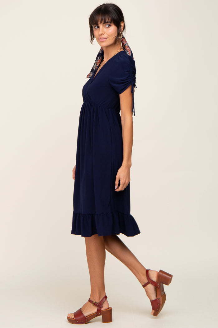 woman wearing a navy blue short sleeve dress with ruffle hem and a patterned scarf tied around her neck