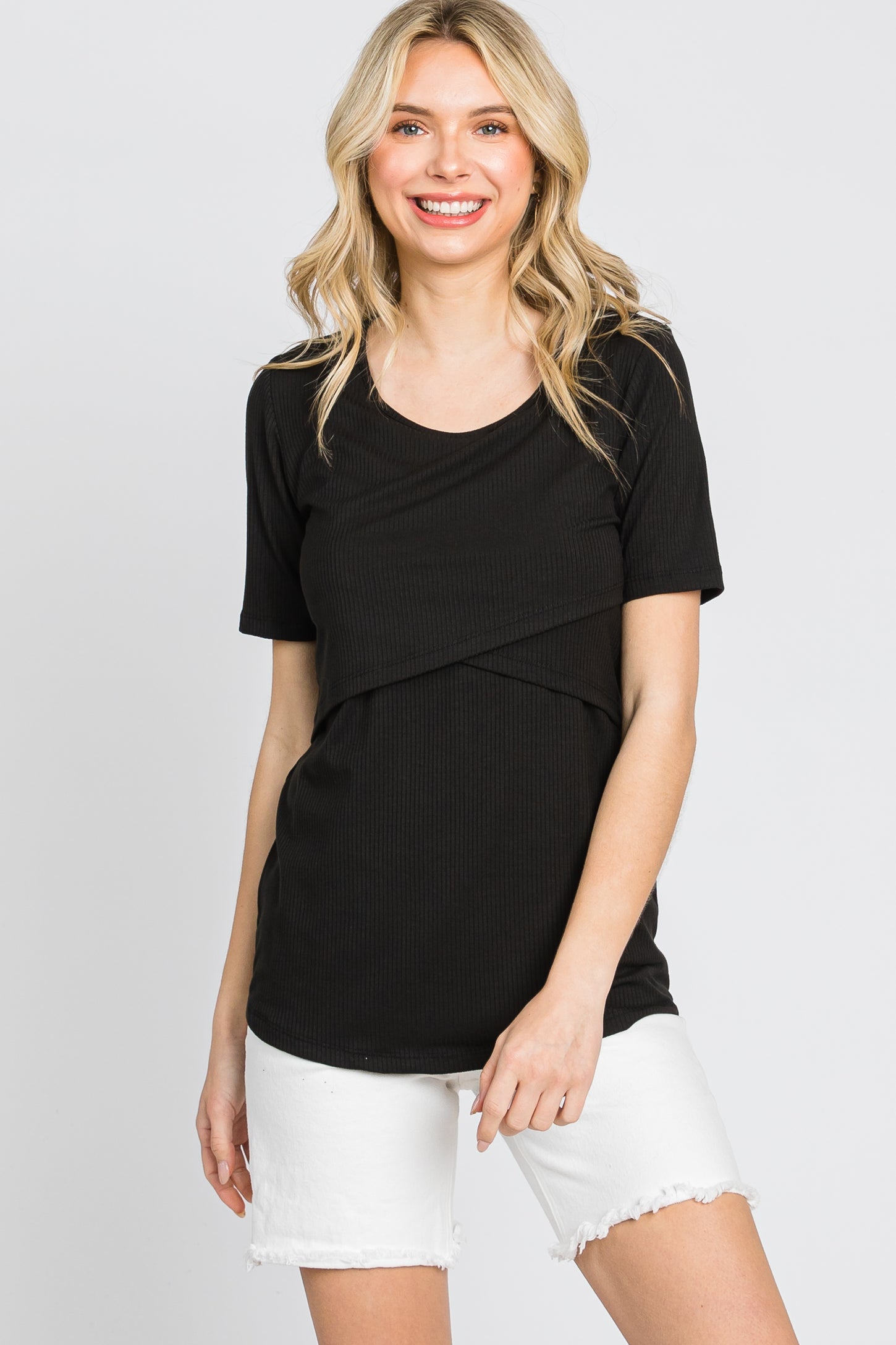 woman wearing a black short sleeve top with a crossover front detail and white denim shorts