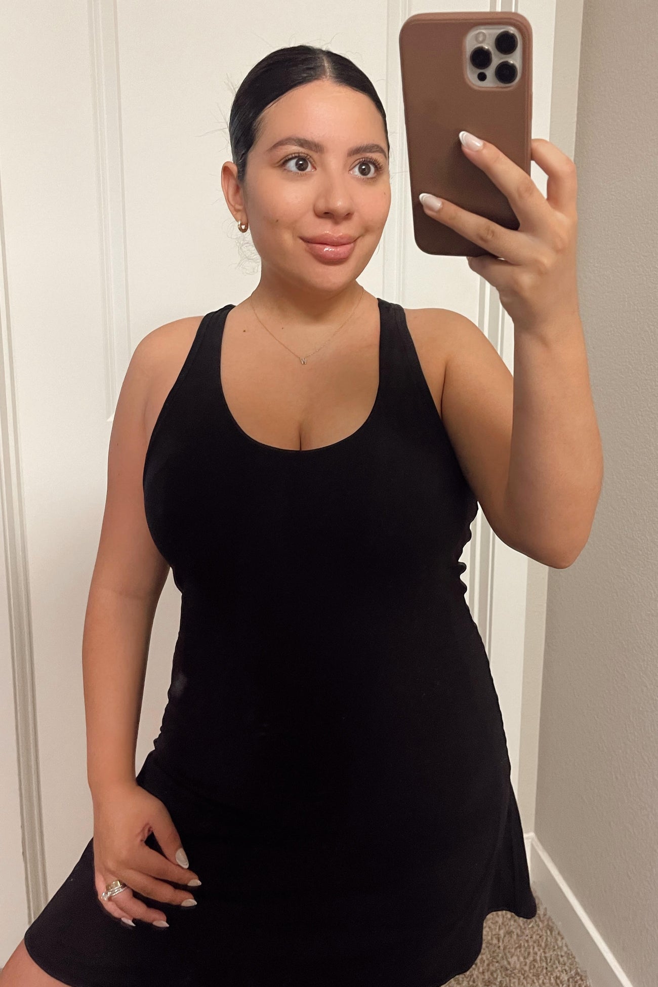 woman wearing a black sleeveless mini dress and taking a mirror selfie