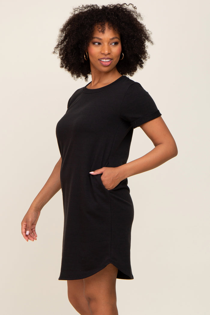 woman wearing a black short sleeve dress with a relaxed fit and side pockets, standing sideways with a smile
