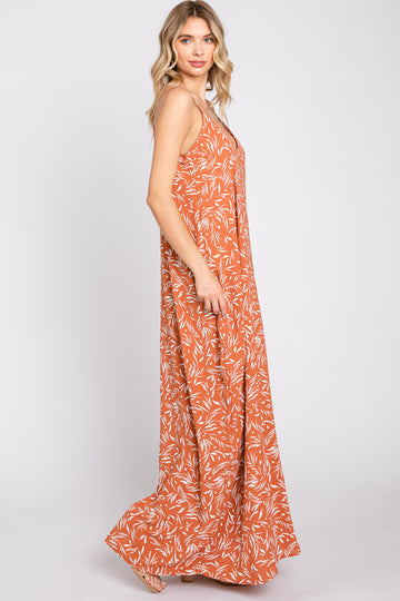 woman wearing an orange maxi dress with a white leaf pattern and spaghetti straps