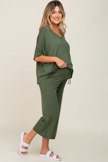 woman wearing a green maternity outfit with a loose top and crop pants, showcasing her baby bump