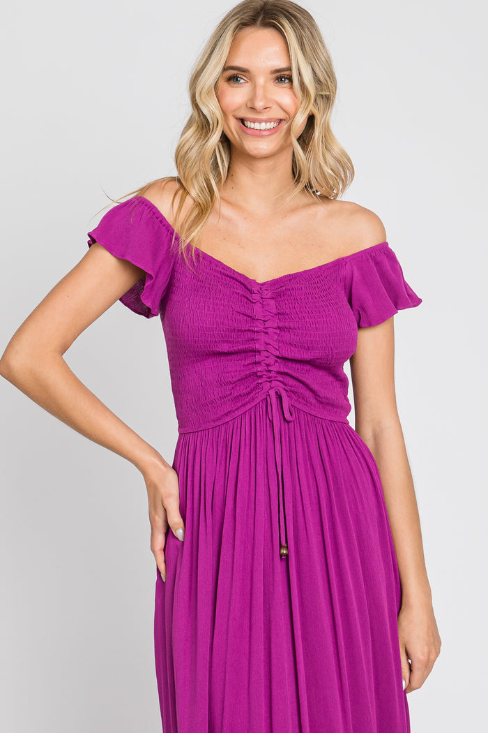 woman wearing a bright purple off-the-shoulder dress with smocked bodice and ruffled sleeves, smiling at the camera