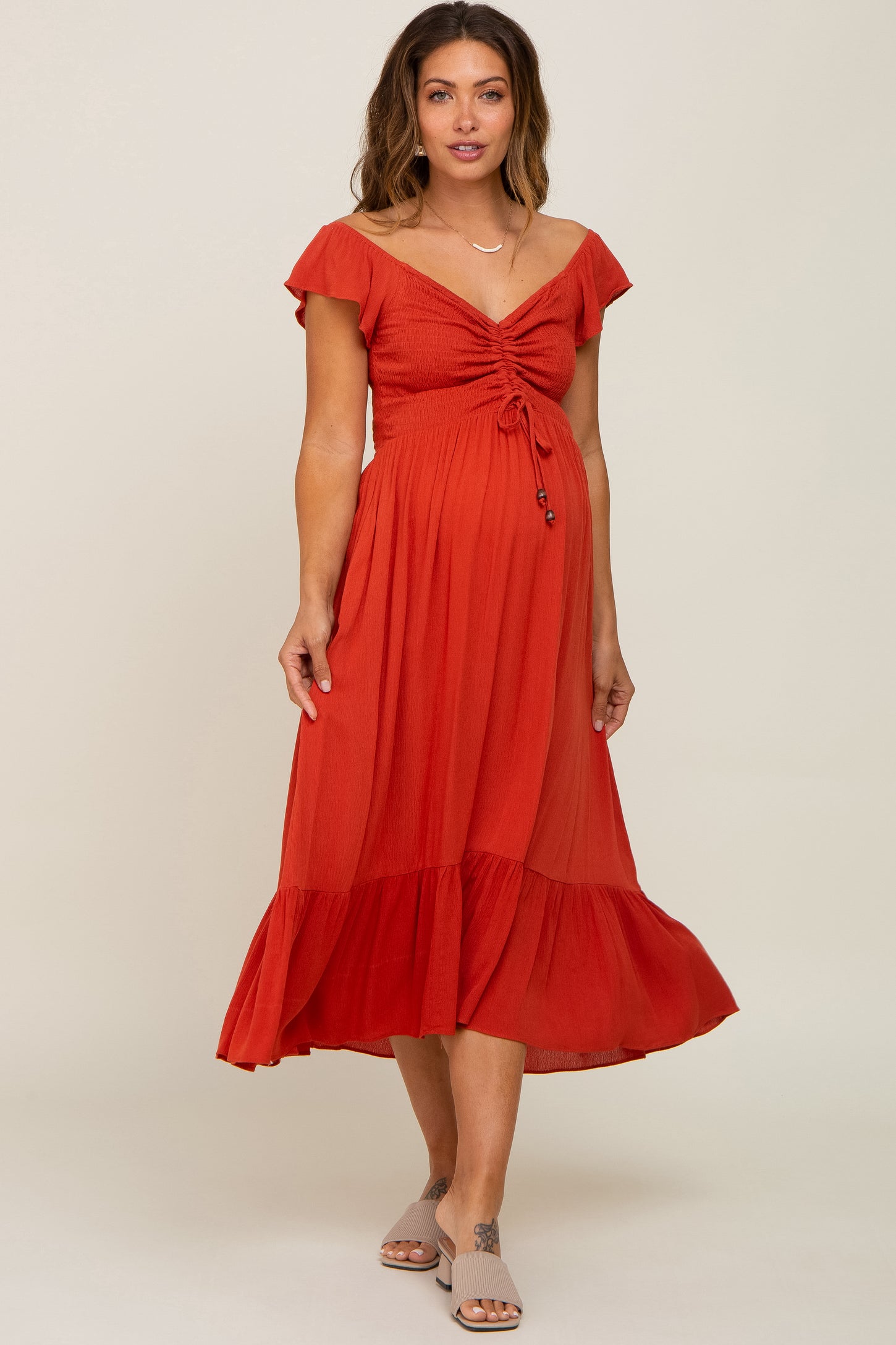 woman wearing a rust red maternity dress with a tie front and flutter sleeves, showcasing her baby bump