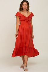 woman wearing a rust red maternity dress with a tie front and flutter sleeves, showcasing her baby bump