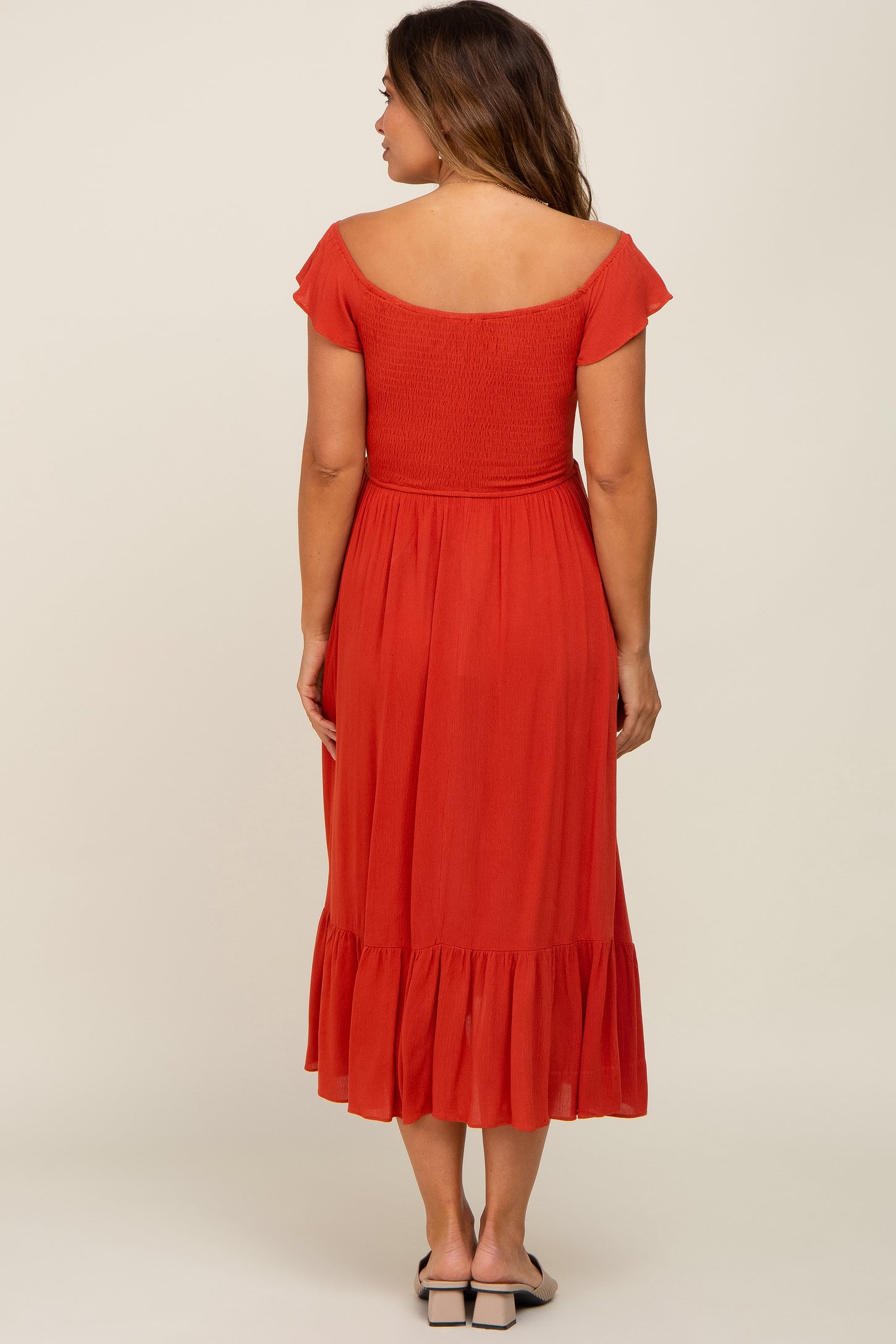 woman wearing a rust red maternity dress with short sleeves and a ruffled hem, showing her baby bump