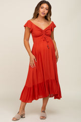 woman wearing a rust red maternity dress with a ruched bodice and flutter sleeves, showing her baby bump