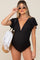 woman wearing a black maternity swimsuit with flutter sleeves and a plunging neckline, holding a straw tote bag and wearing sunglasses