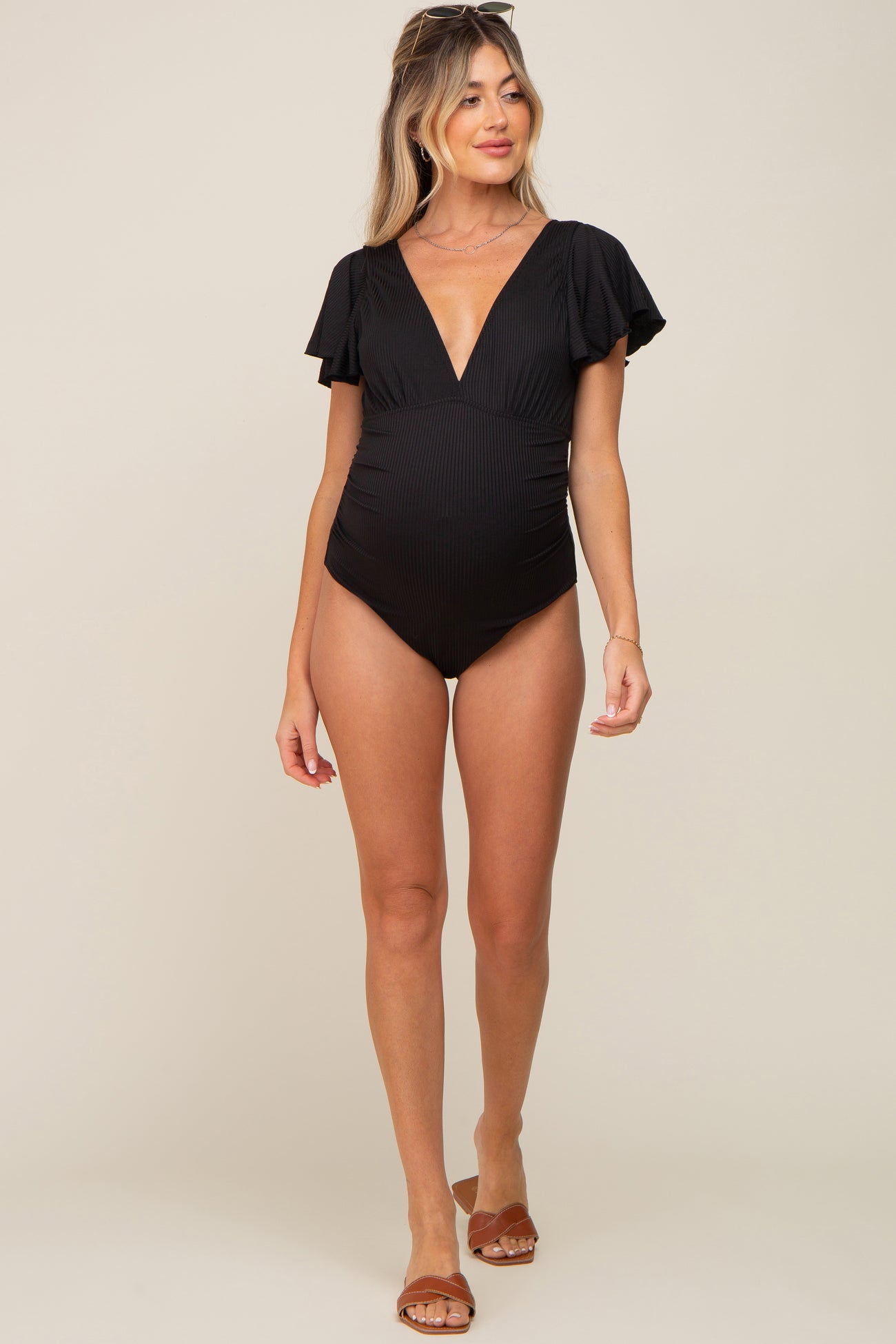 woman wearing a black striped maternity swimsuit with flutter sleeves and a deep v-neck, showing her baby bump