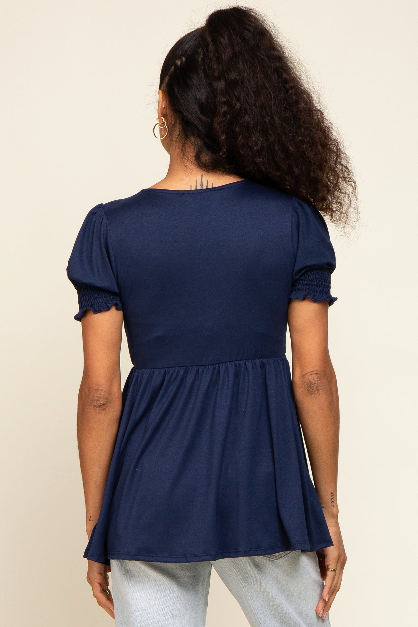 woman wearing a navy blue peplum top with short smocked sleeves, viewed from the back