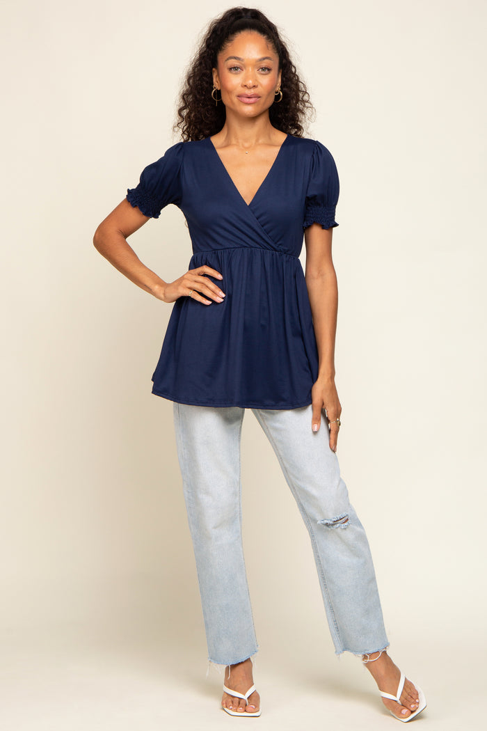 woman wearing a navy blue wrap top with puff sleeves paired with light wash distressed jeans