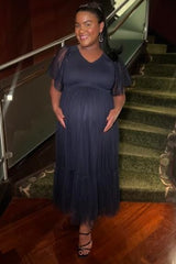 woman wearing a navy blue maternity gown with short tulle sleeves and a flowing skirt, holding her baby bump