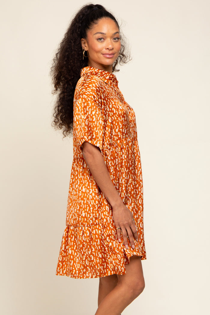 woman wearing an orange short sleeve patterned dress with a tiered skirt and collared neckline