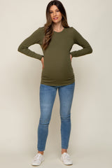 woman wearing a dark green long sleeve maternity top and showing her baby bump, paired with light blue skinny jeans
