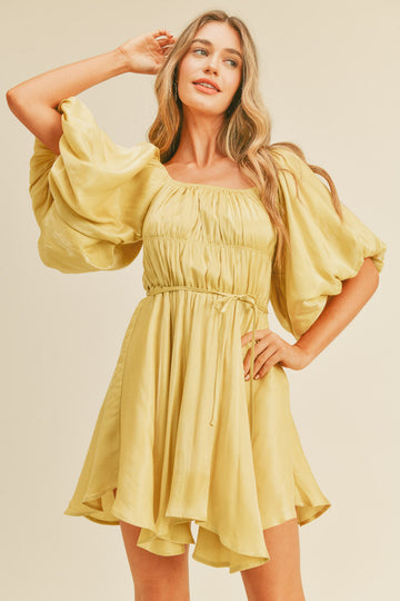 woman wearing a light yellow short dress with puff sleeves and a cinched waist, styled with a relaxed fit