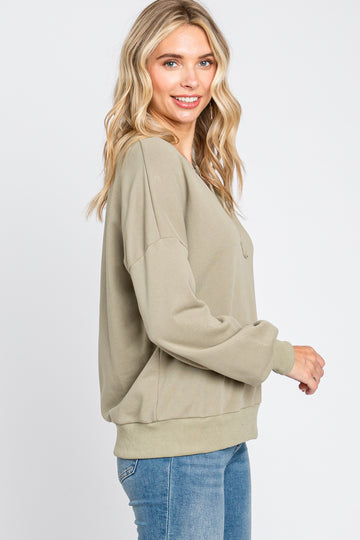woman wearing olive green oversized sweatshirt and blue jeans against a white background