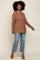 woman wearing a relaxed fit brown knit sweater and light blue distressed jeans, standing with a smile