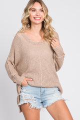 woman wearing a beige loose-knit sweater with a scoop neckline and side slits, paired with distressed denim shorts