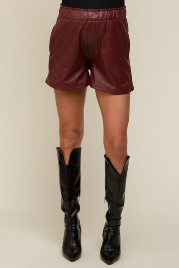 woman wearing burgundy faux leather maternity shorts paired with black knee-high boots