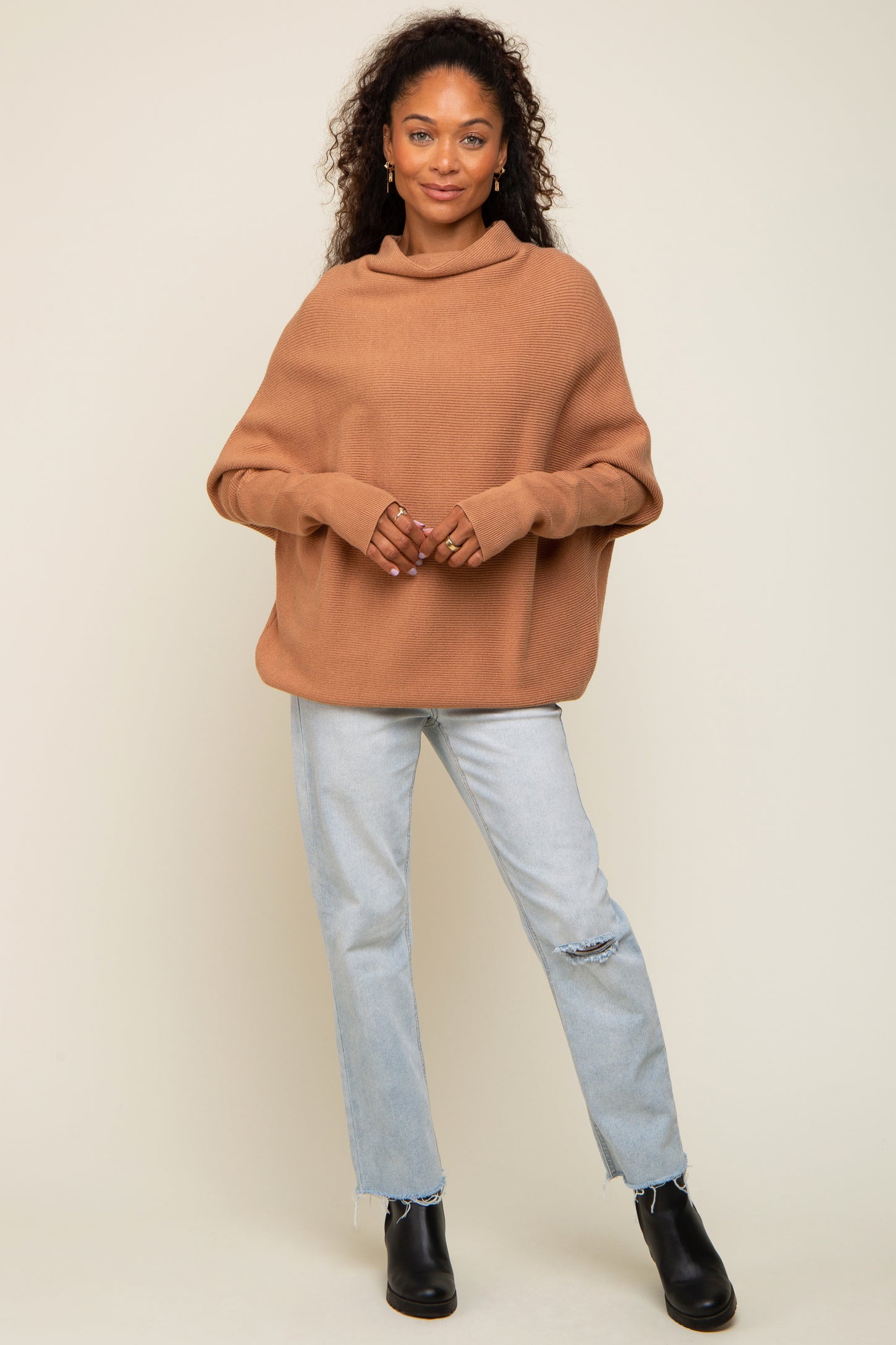 woman wearing a cozy brown oversized sweater with a cowl neck and light blue distressed jeans
