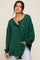 woman wearing a green oversized henley shirt with a pocket and button details, paired with light blue jeans