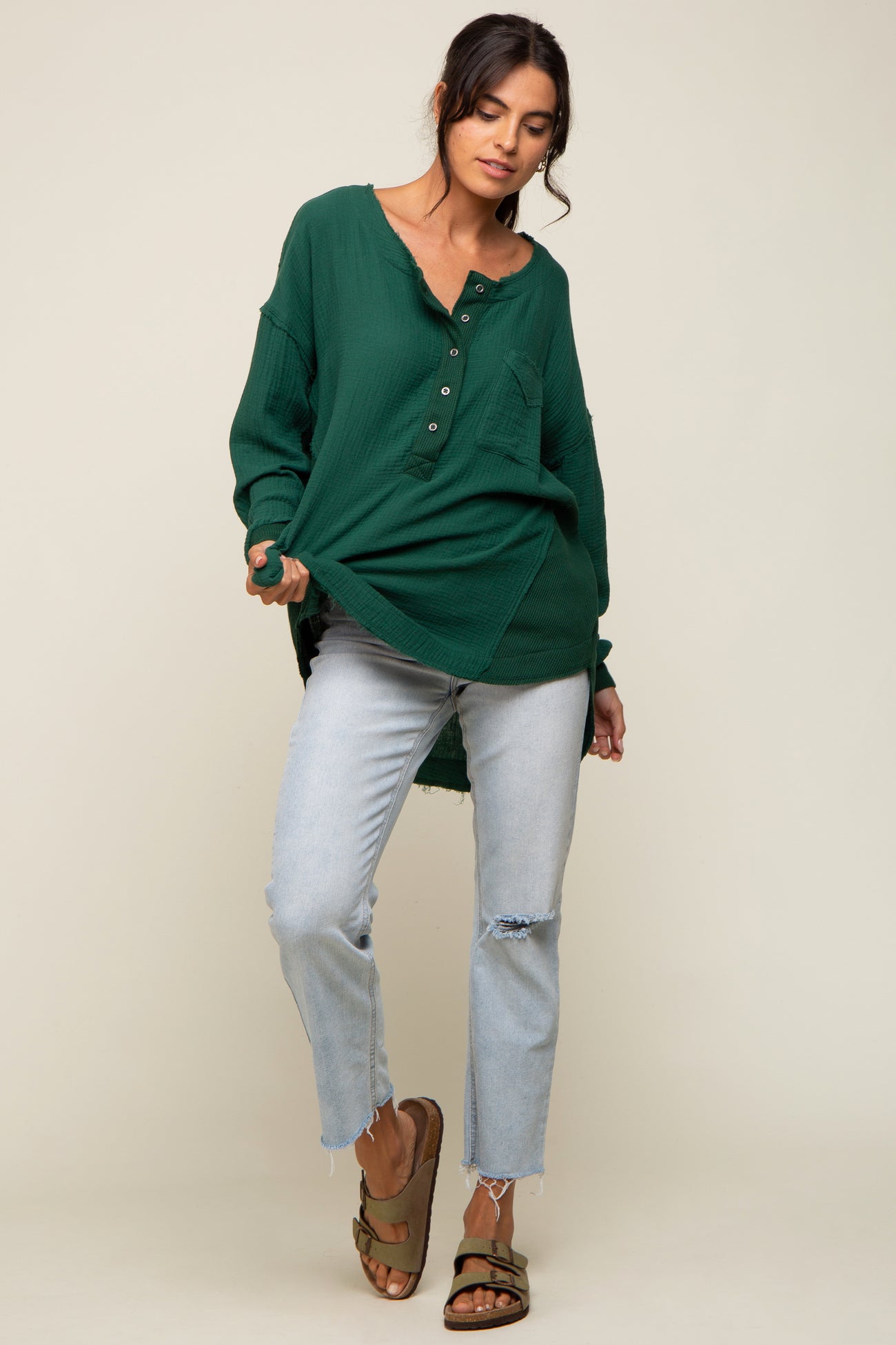 woman wearing a dark green oversized button-up shirt and light blue ripped jeans, standing with one hand on her hip