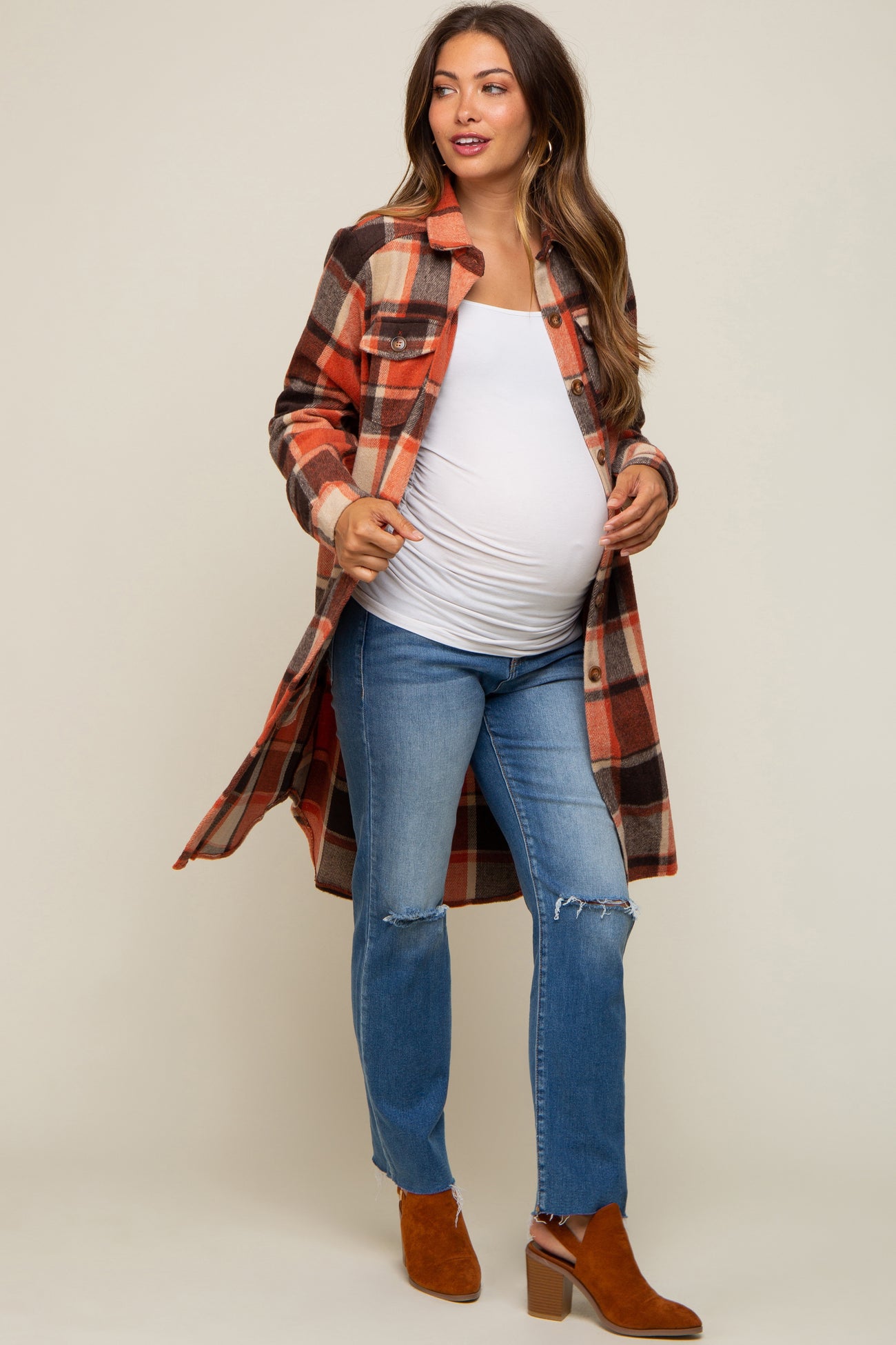 woman wearing a plaid maternity shacket over a white maternity tank top, with a visible baby bump and paired with distressed jeans and ankle boots