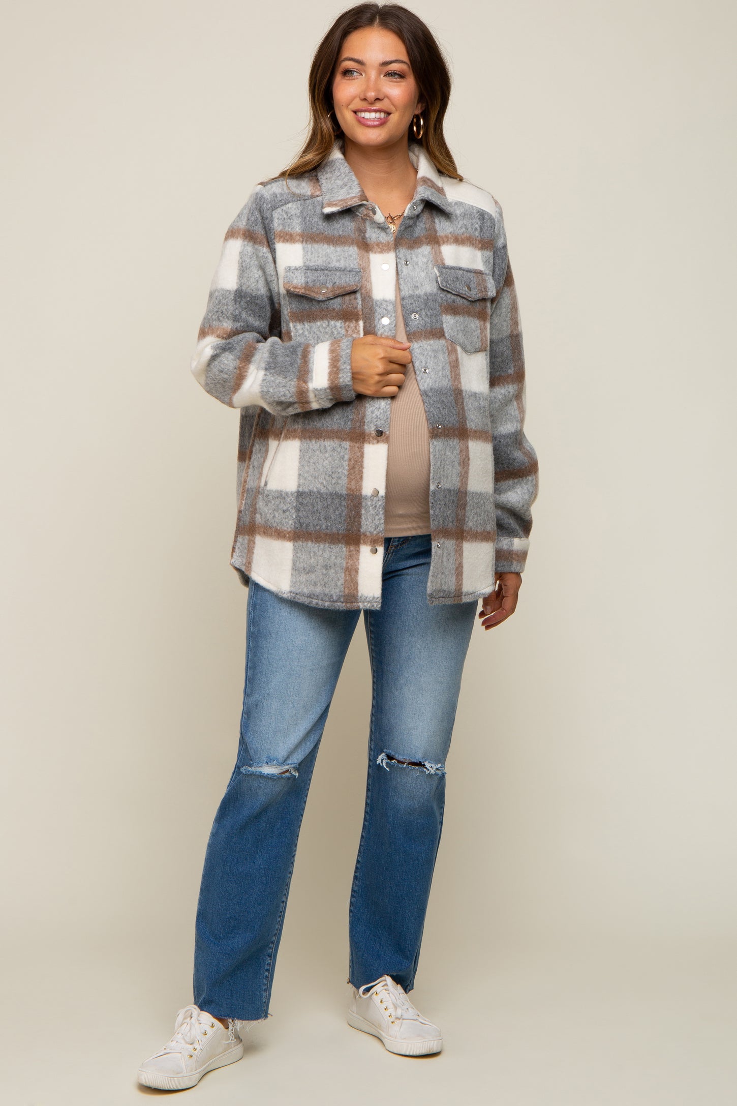woman wearing a gray and white checkered maternity shacket with a light top and distressed jeans, showing her baby bump
