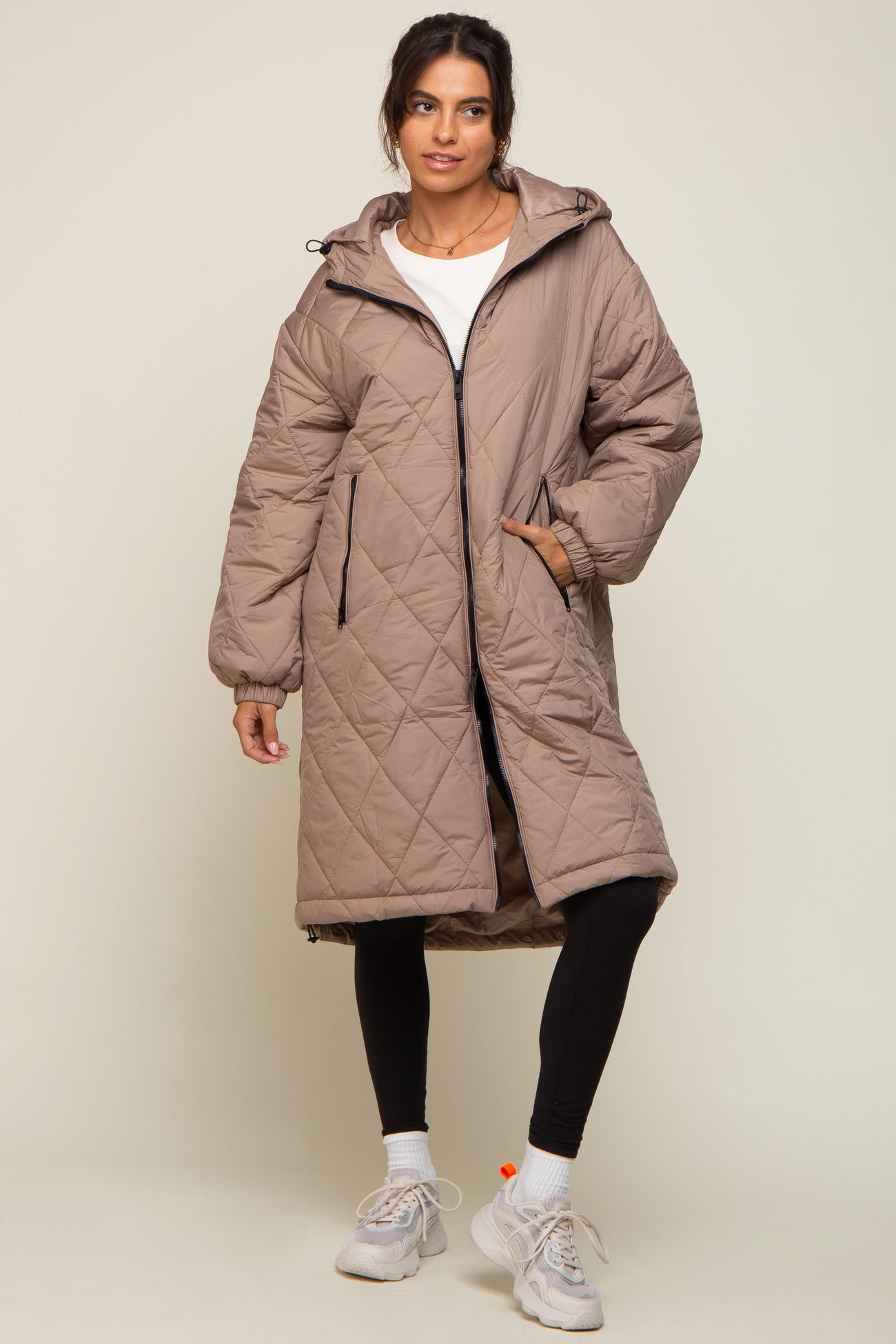 woman wearing a beige quilted puffer coat with a hood and zip closure, paired with black leggings and sneakers