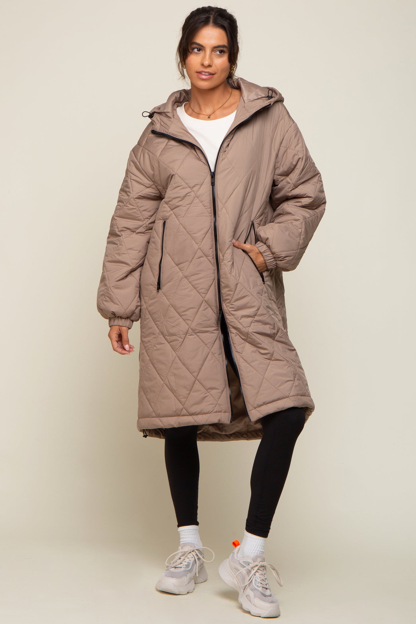woman wearing a beige quilted puffer coat with a hood and zip closure, paired with black leggings and sneakers