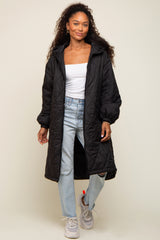woman wearing a black quilted long coat over a white top and light blue jeans, standing in casual sneakers