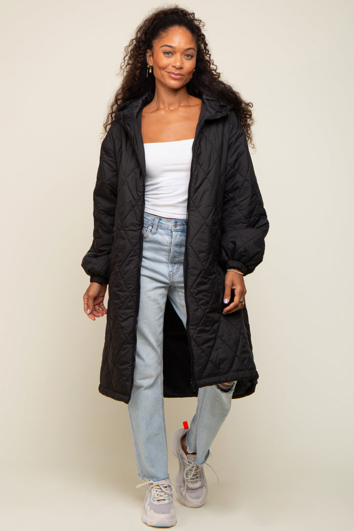 woman wearing a black quilted long coat over a white top and light blue jeans, standing in casual sneakers