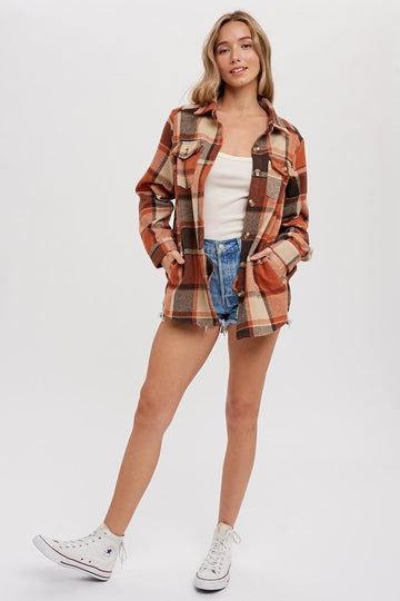 woman wearing an orange and brown plaid shacket over a white top and denim shorts, standing with one leg forward
