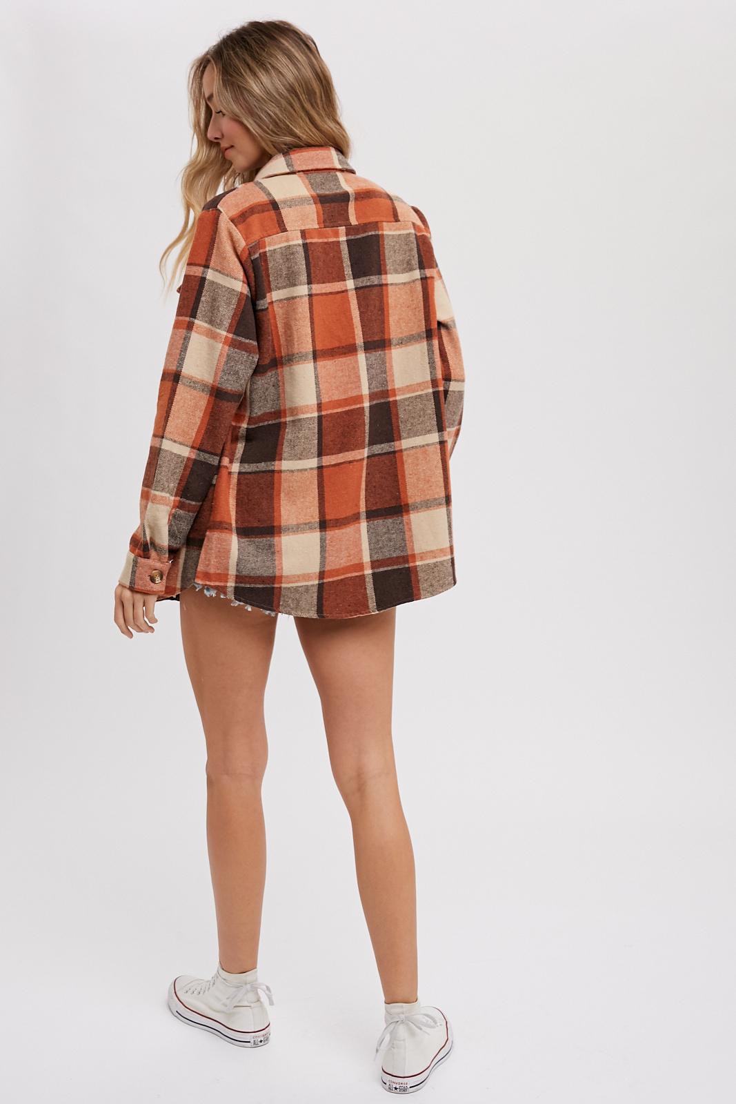 woman wearing an orange and brown plaid oversized flannel shirt, seen from the back, paired with denim shorts and white sneakers