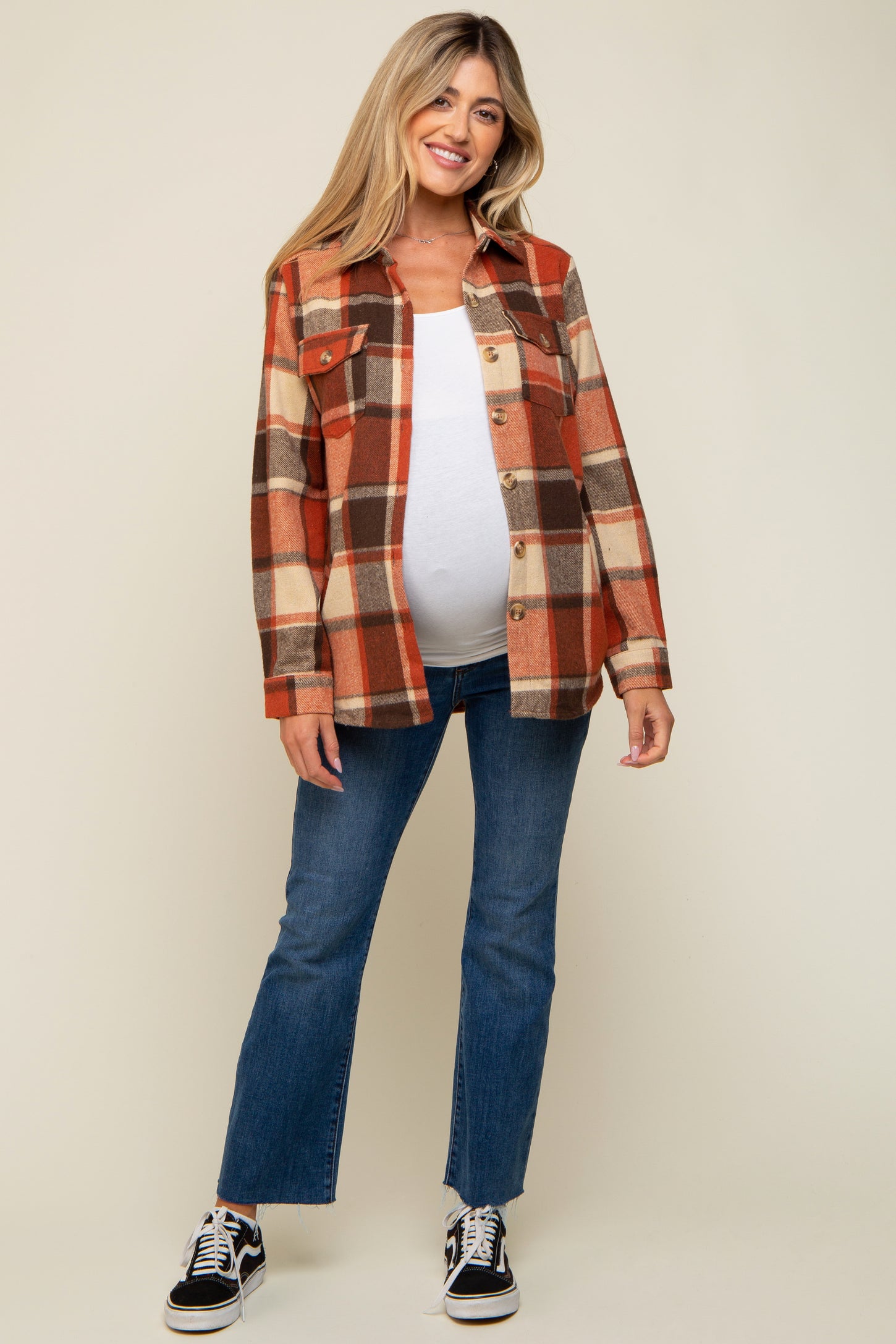 woman wearing a rust and cream plaid maternity shacket with a visible baby bump and flare jeans
