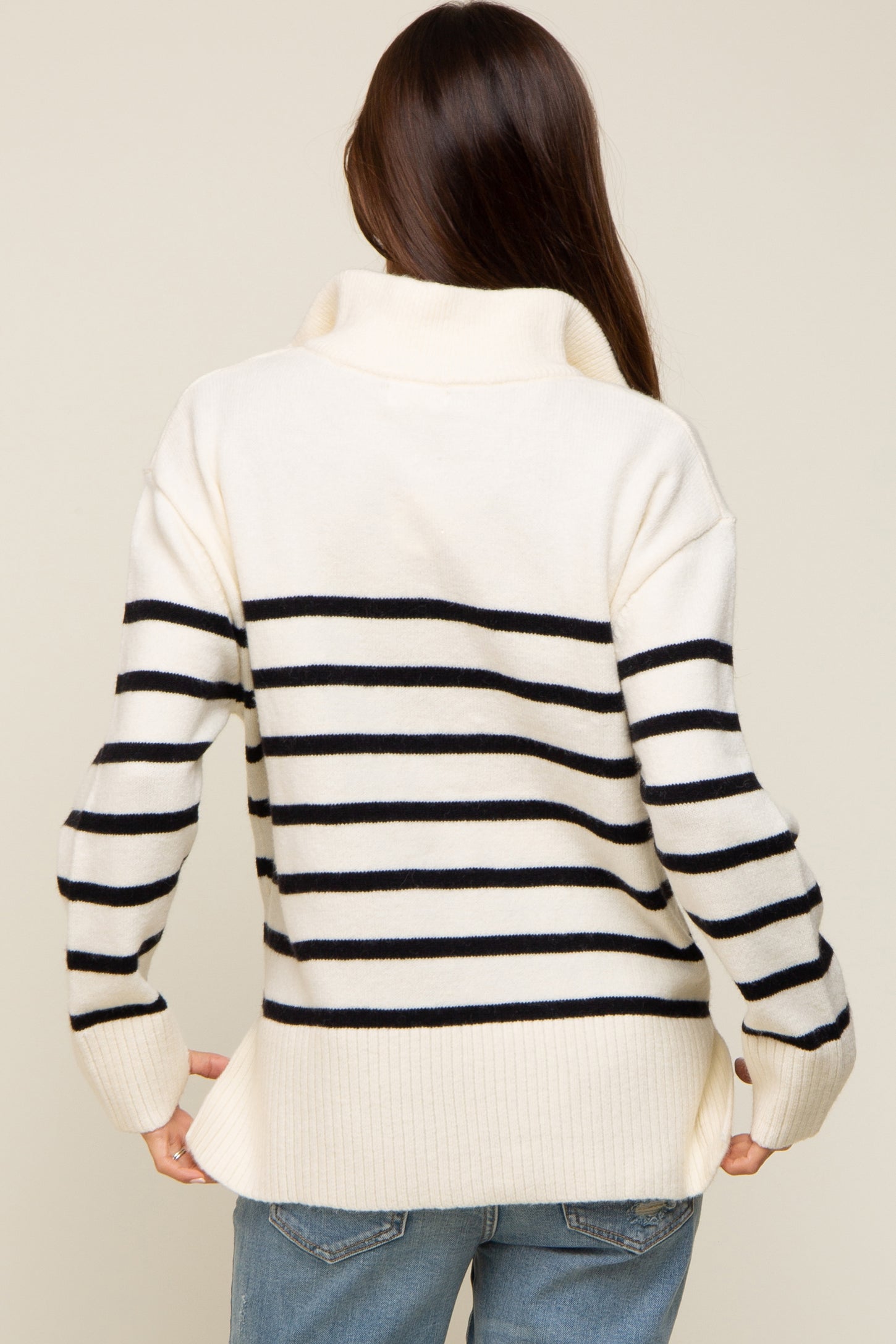 woman wearing a cream and black striped maternity sweater with a high neckline and relaxed fit, showing her baby bump