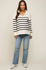 woman wearing a cream and black striped maternity sweater with a zip collar and light blue ripped jeans
