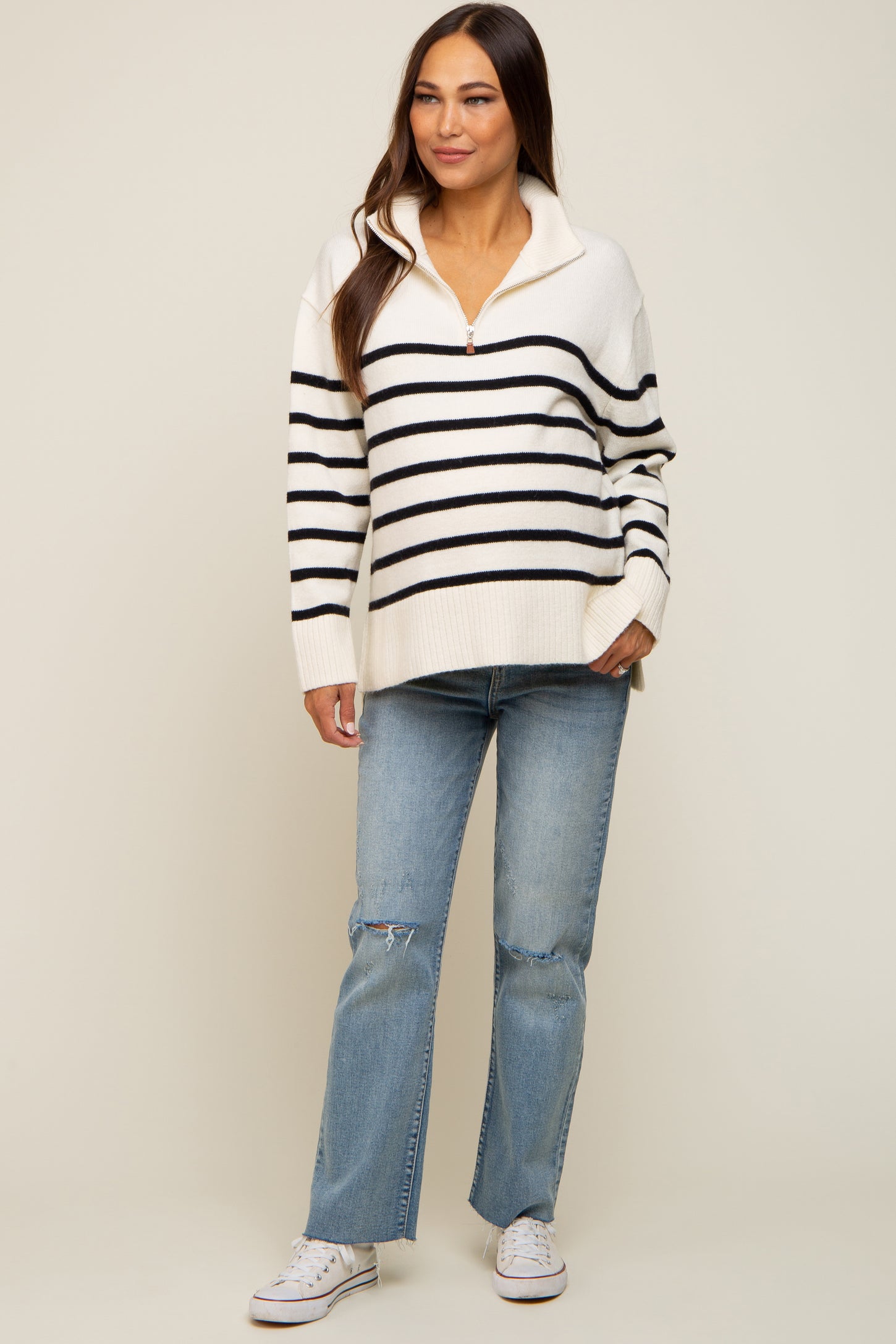 woman wearing a striped cream and black maternity pullover sweater with a quarter zip and distressed light blue jeans