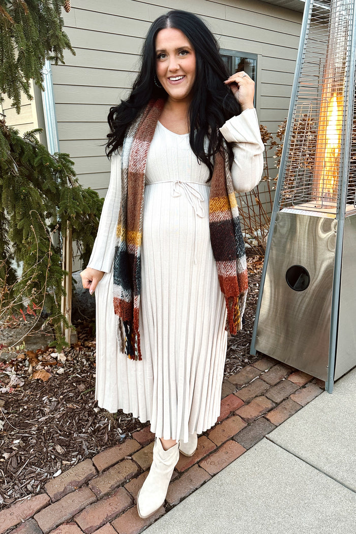 woman wearing a cream long sleeve pleated dress with a tie waist and a multicolored scarf, styled with beige boots