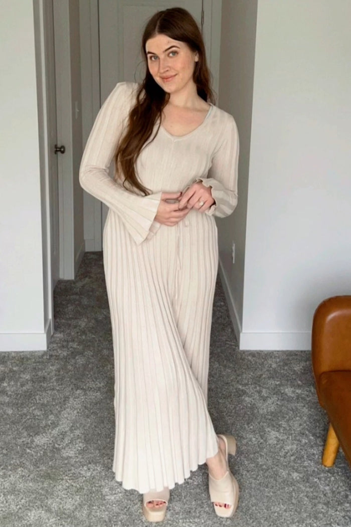 woman wearing a beige ribbed maxi dress with long bell sleeves and buttons, posing in a bright room