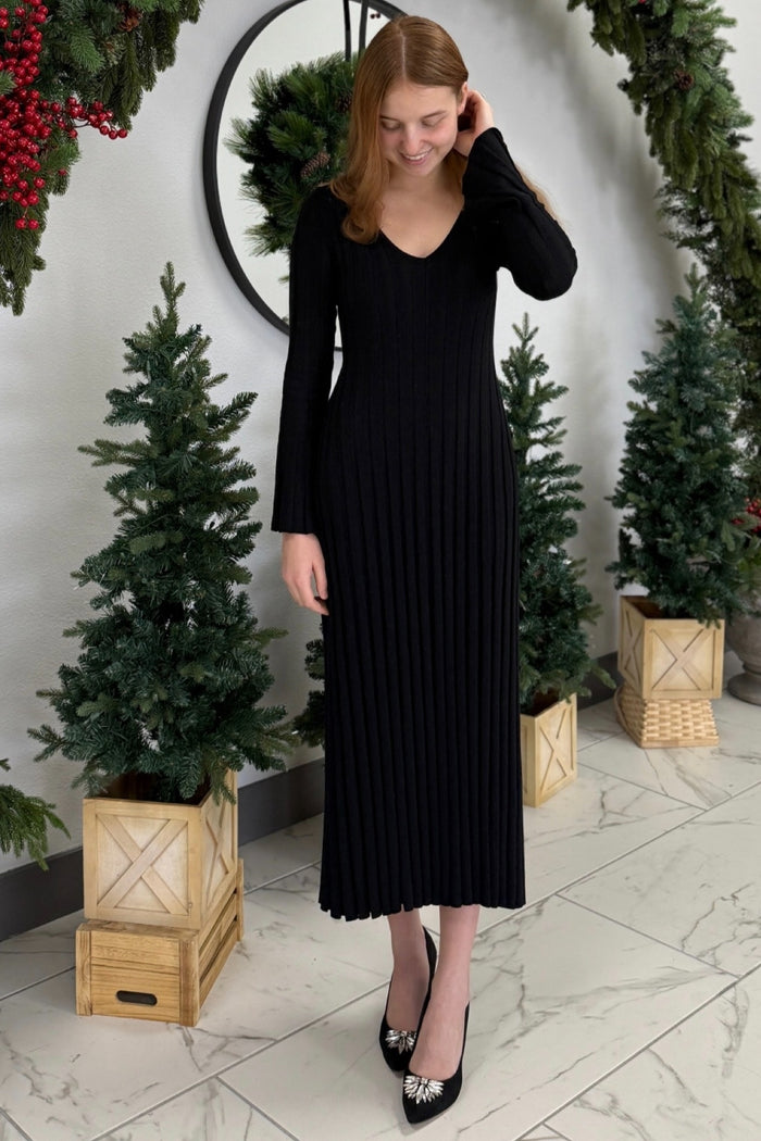 woman wearing a black ribbed long sleeve maxi dress with a v-neckline and standing among holiday decorations