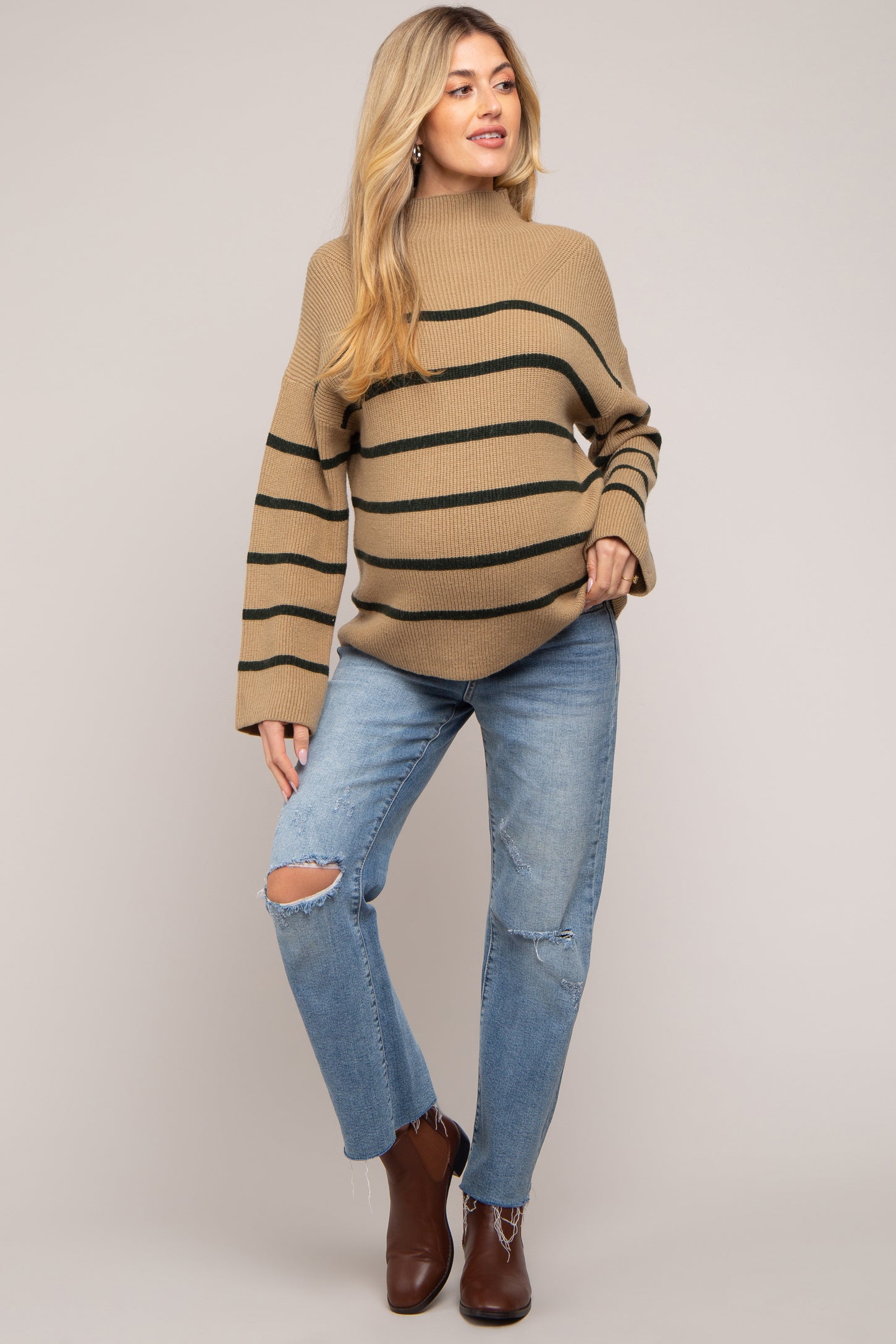 woman wearing a beige and green striped maternity sweater and distressed jeans, showing her baby bump